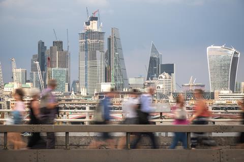 Blurred passers-by walk in front of the London City skyline