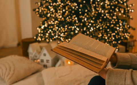An open book is held in front of a Christmas tree