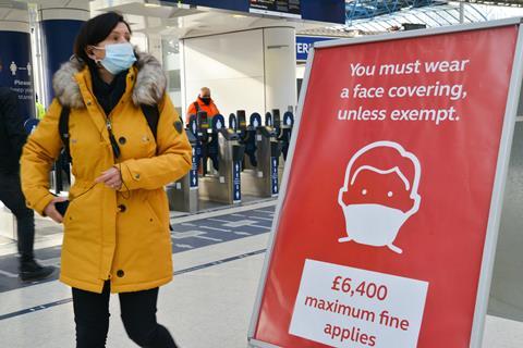 A commuter wearing a face mask walks past a sign at London Waterloo train station reminding the public they can be fined for not wearing one