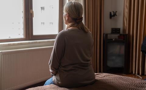 An older woman looks out of her bedroom window