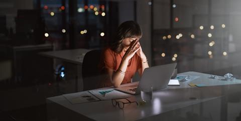 A woman sits at her office desk late at night with her head in her hands