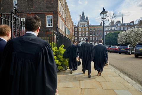A group of barristers in robes walk together, holding their wigs