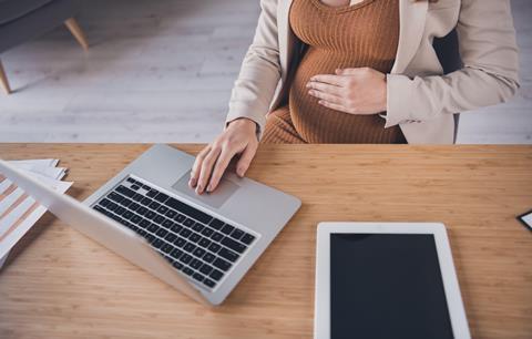 An anonymous pregnant woman sits at a desk and works from a laptop