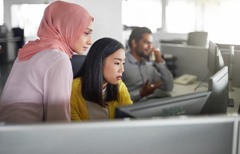 A young office worker helps out a colleague at a computer