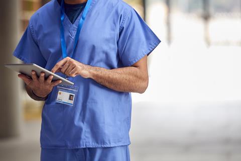 An anonymous doctor in hospital scrubs checks a tablet