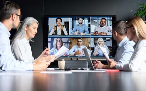 A group of four colleagues sit round a table while listening to clients on a virtual call