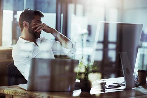 A tired man puts his hands over his eyes while sat at his desk