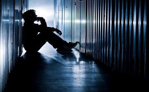 The silhoutte of a young man sits on the floor of a cell