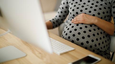 A pregnant woman rests her hand on her bump as she works on her computer