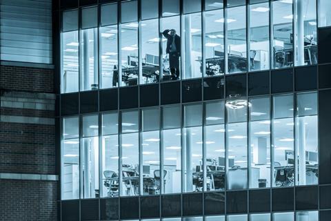 A man alone in the office looks out of a window at night