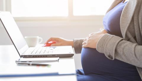 A pregnant woman rests her hand on her baby bump as she works at a laptop