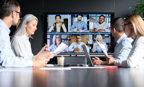 A group of four colleagues sit round a table while listening to clients on a virtual call