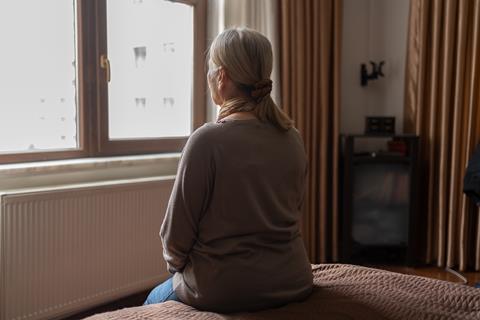 An older woman looks out of her bedroom window