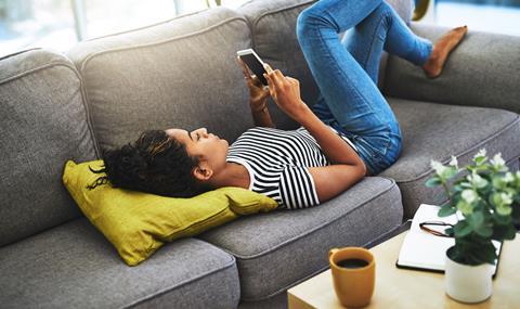 A woman lies on the sofa scrolling on her phone