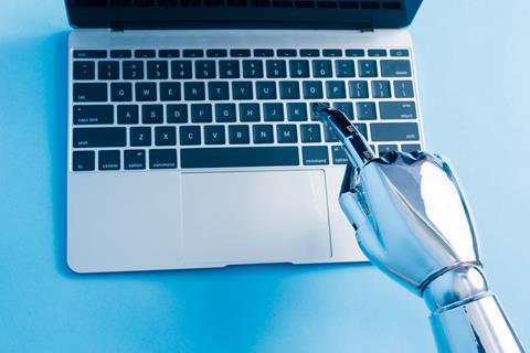 A robot hand types on a laptop keyboard