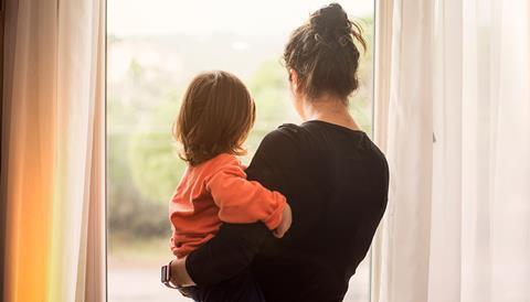 A mother holds her toddler as they look out the window