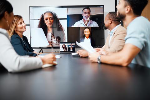 Four colleagues in an office meeting room chat to coworkers on screen