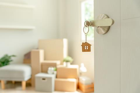 A house keyring hangs from a key in a lock, showing moving boxes behind the open door