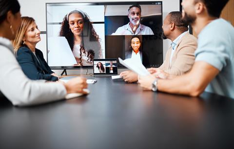 Four colleagues in an office meeting room chat to coworkers on screen