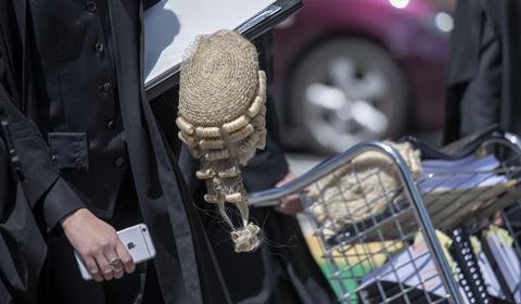 An anonymous barrister wearing a robe carries a barrister wig into court