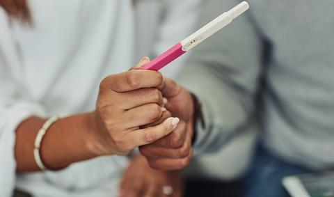 An anonymous couple hold hands as they read a pregancy test