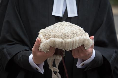 An anonymous barrister holds their wig in front of them