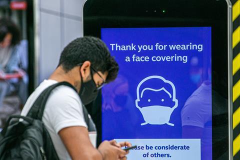 A traveler wearing mask at Waterloo station stands in front of a Covid safety sign