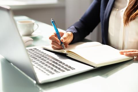 A woman takes notes while studying a laptop