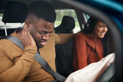 A couple in a car hold their necks in pain