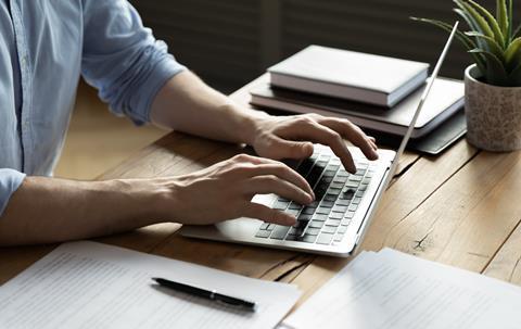 A close up of a man sat at a desk and typing on his laptop