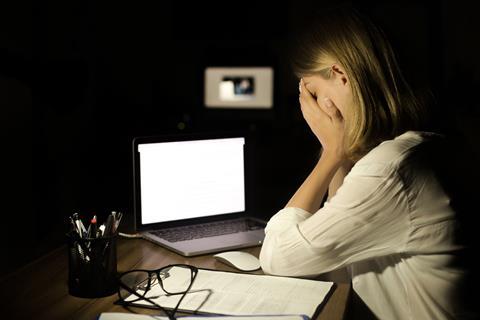 A young woman sits with her head in her hands in front of a laptop in a dark office