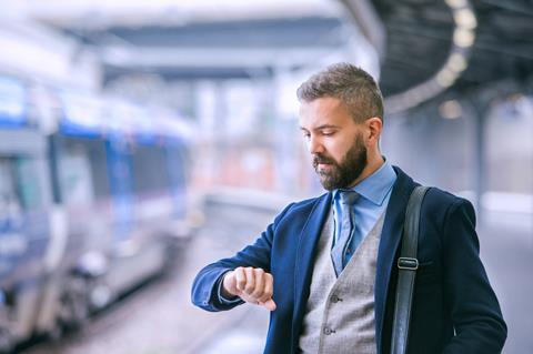 A man looks at his watch as he waits for a train on a station platform