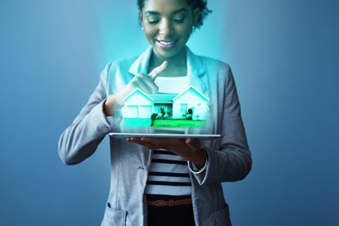 A woman looks down at a virtual house projected from the screen of a tablet