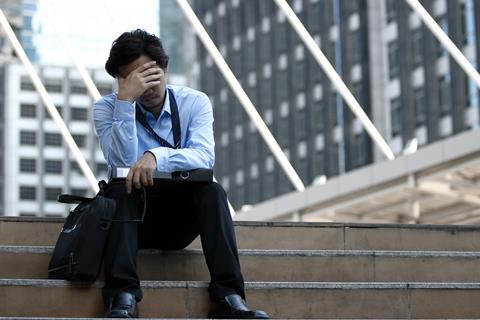 A young man sits on steps outside his office with his head in his hands