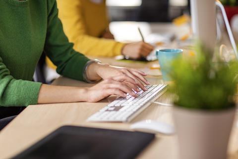 Anonymous young woman types on computer keyboard next to colleague in office