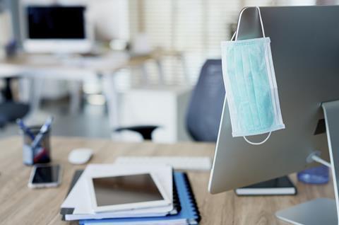 A face mask hangs off the back of a computer screen on an office desk