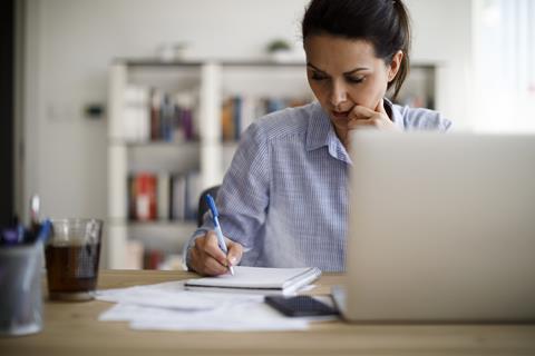 A woman writes in a notepad as she sits in front on a laptop