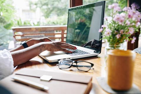 Woman types on laptop at kitchen table