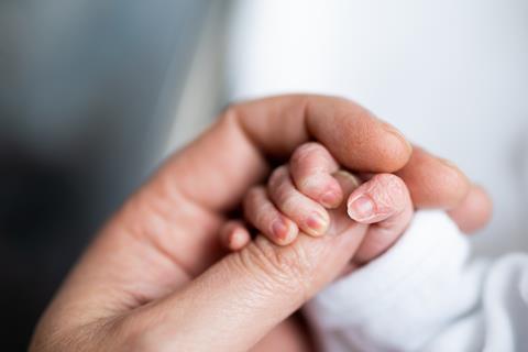 A newborn baby clasps hold of their parent's thumb