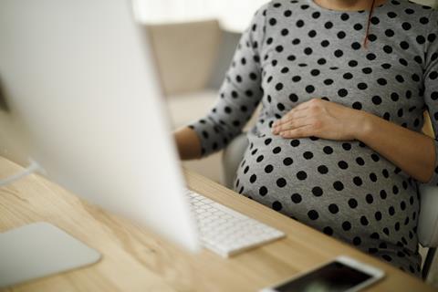 A pregnant woman rests her hand on her bump as she works on her computer