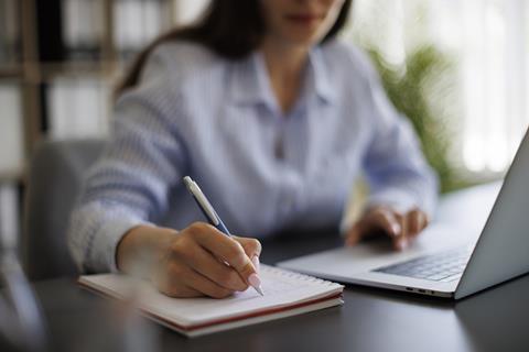 A solicitor takes notes while working on laptop