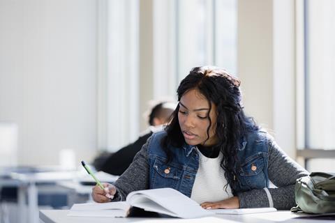 Female student writes notes while reading textbook